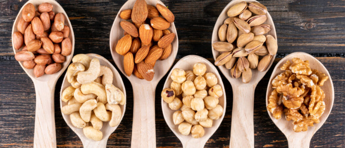 Some of assorted nuts and dried fruits with pecan, pistachios, almond, peanut, cashew, pine nuts in a wooden spoons on wooden background, top view.